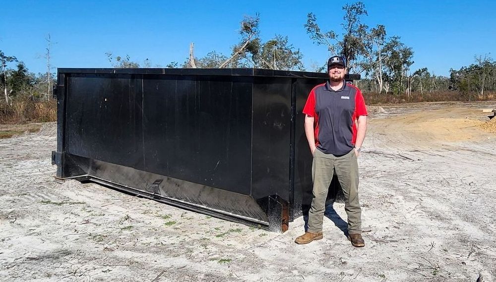 A large black dumpster is sitting in the middle of a field in McAlpin, Florida