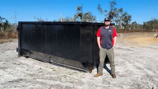A large black dumpster is sitting in the middle of a field in McAlpin, Florida
