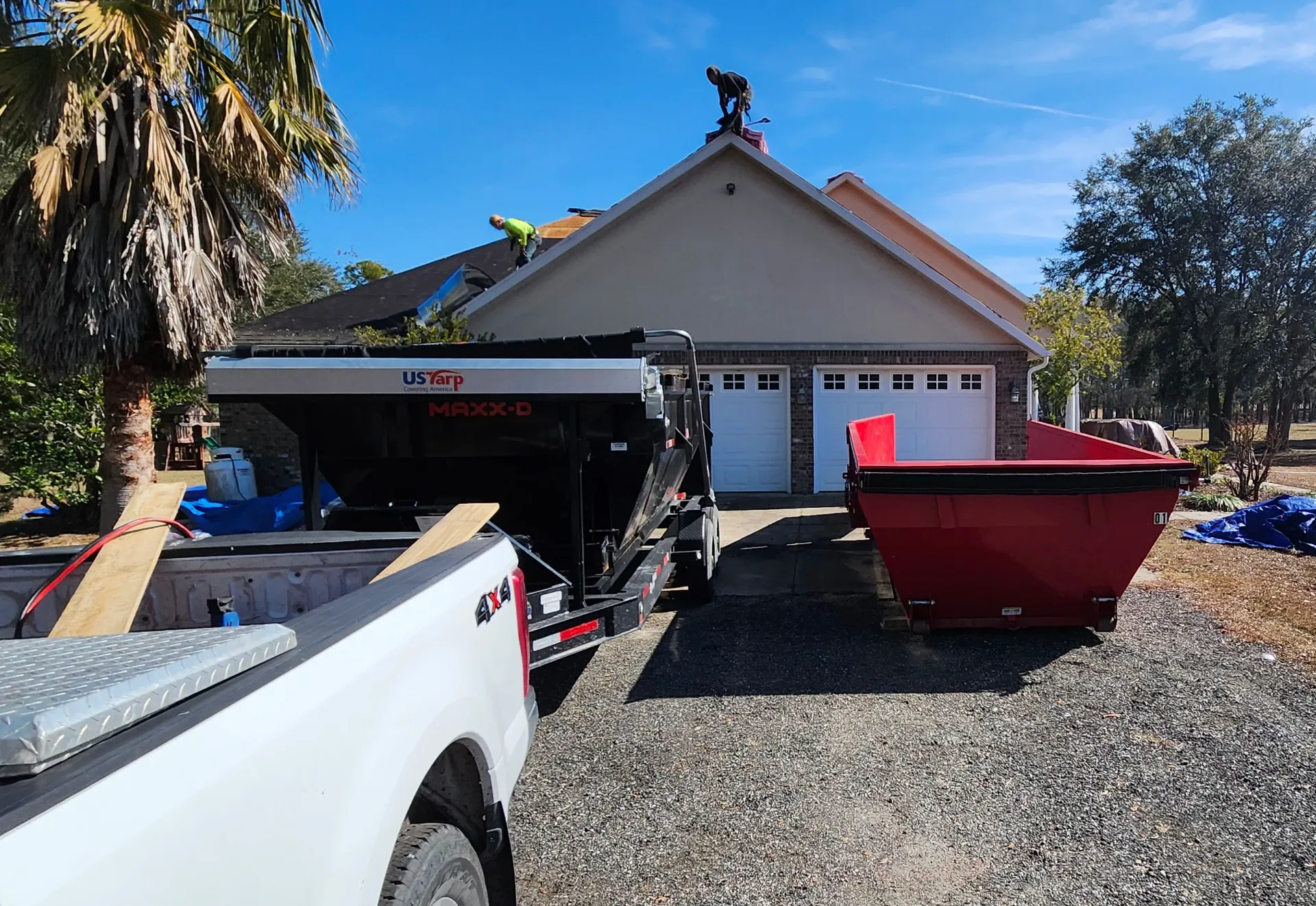 A white truck is parked in front of a house with a dumpster in the driveway.