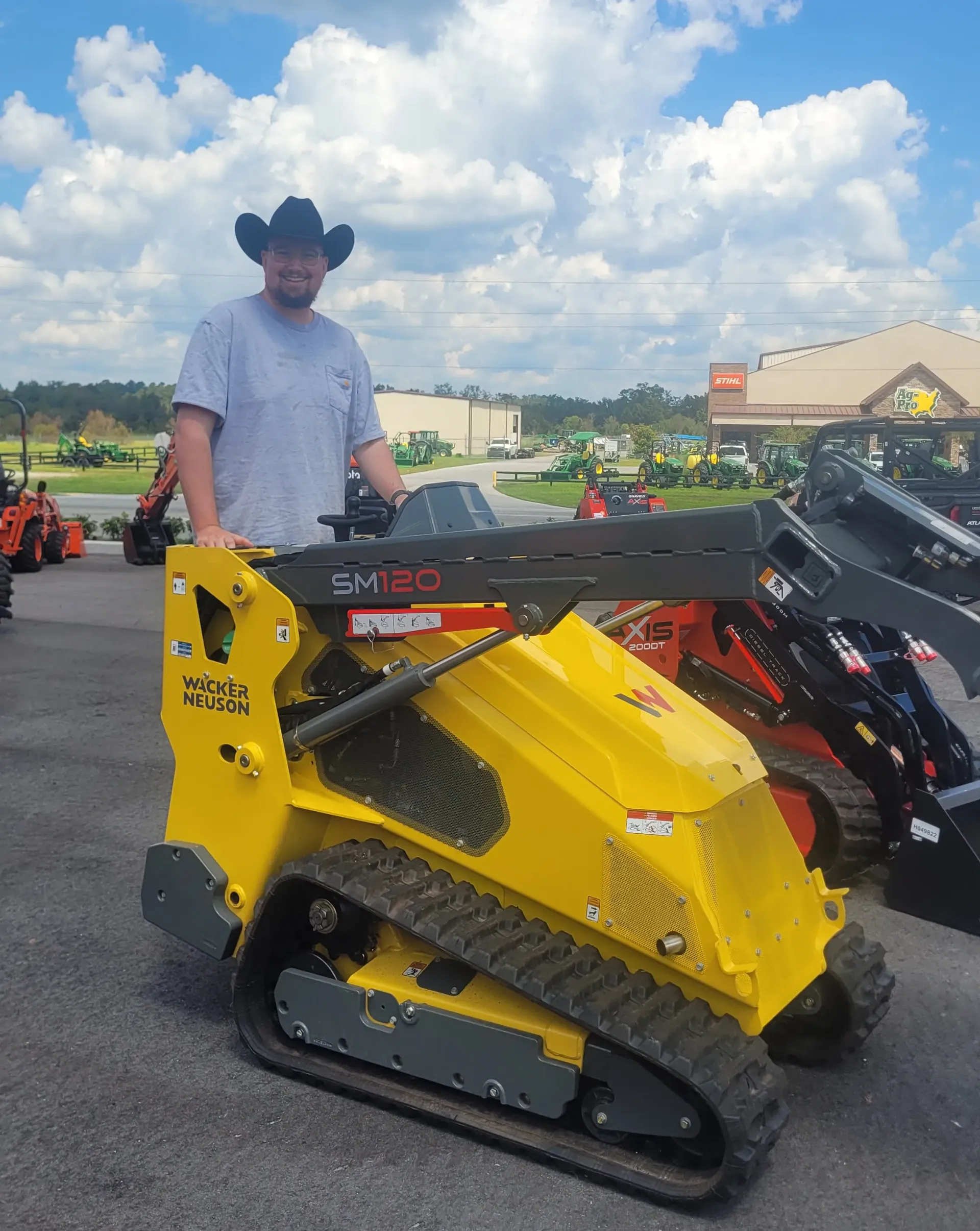 A man in a cowboy hat is standing next to a yellow rental skid steer in Live Oak, Florida