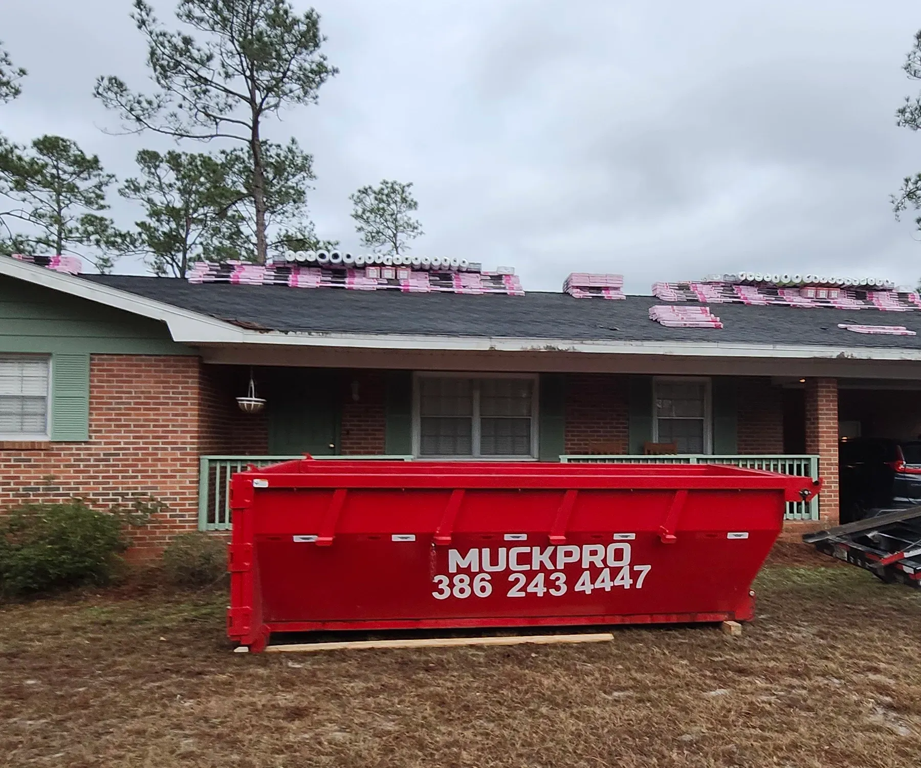 A red muckpro dumpster sits in front of a house