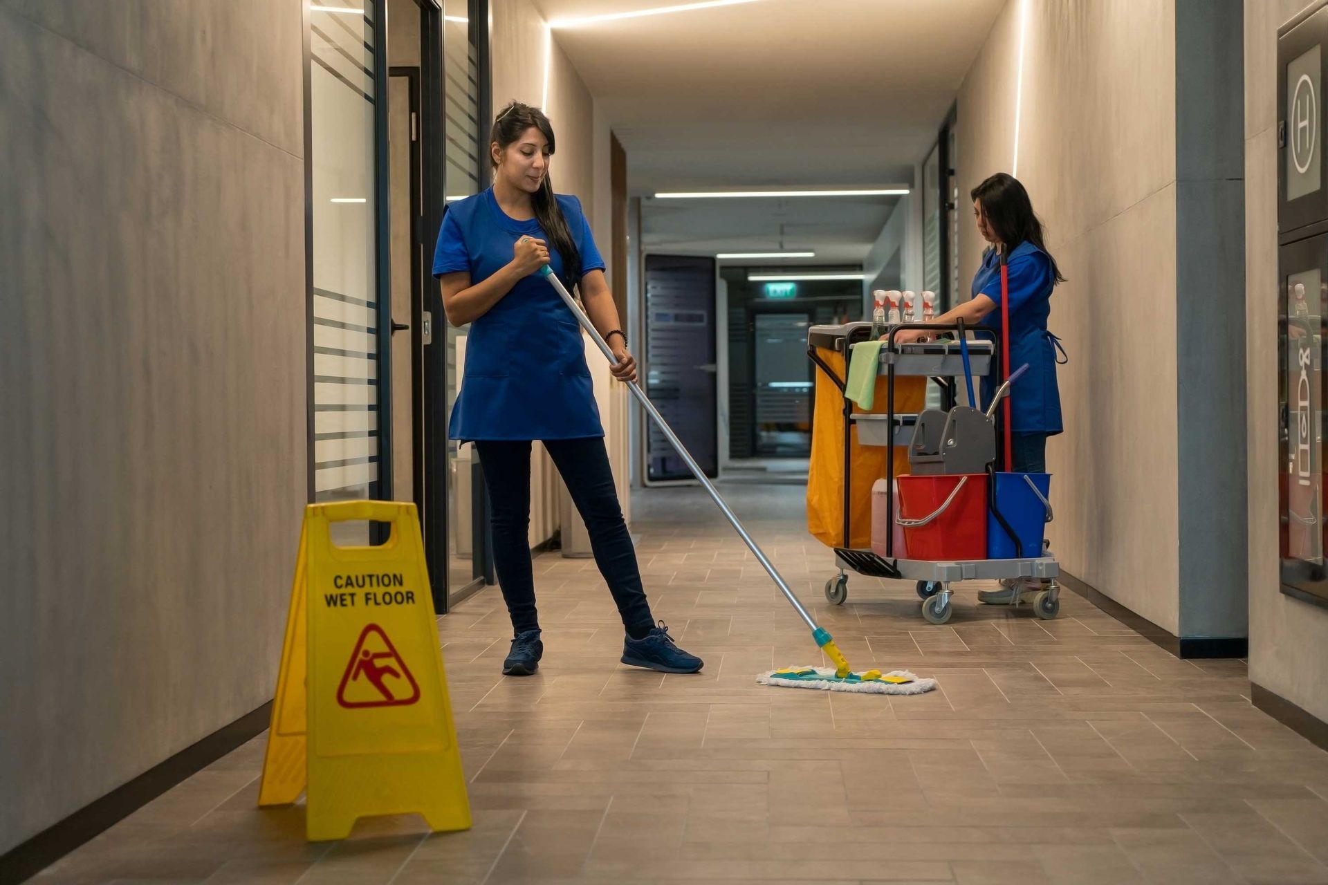 Janitorial staff carefully mopping floor beside caution sign for safety. Janitorial staff carefully mopping floor beside caution sign for safety.