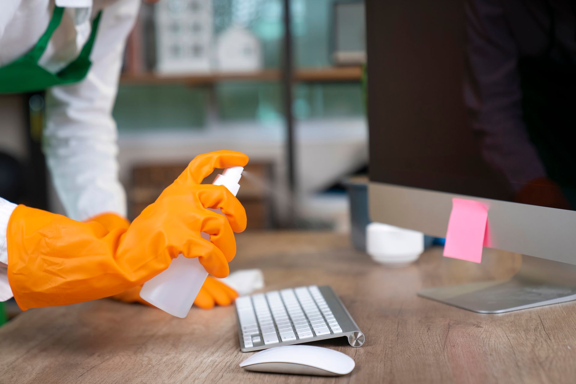A woman is inspecting an office desk with a sponge and spray cleaner.