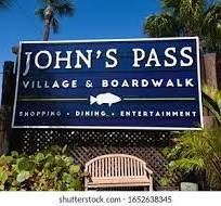 A sign for john 's pass village and boardwalk with a bench in front of it.