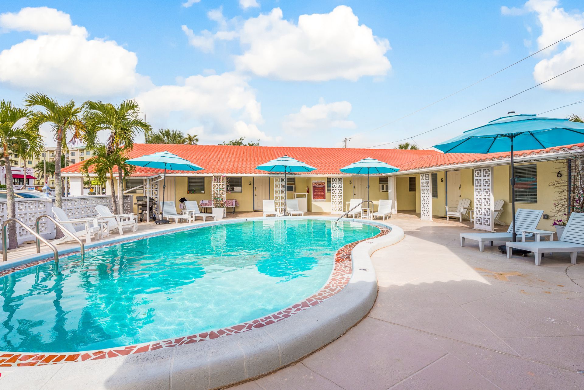 A large swimming pool surrounded by chairs and umbrellas in front of a hotel.