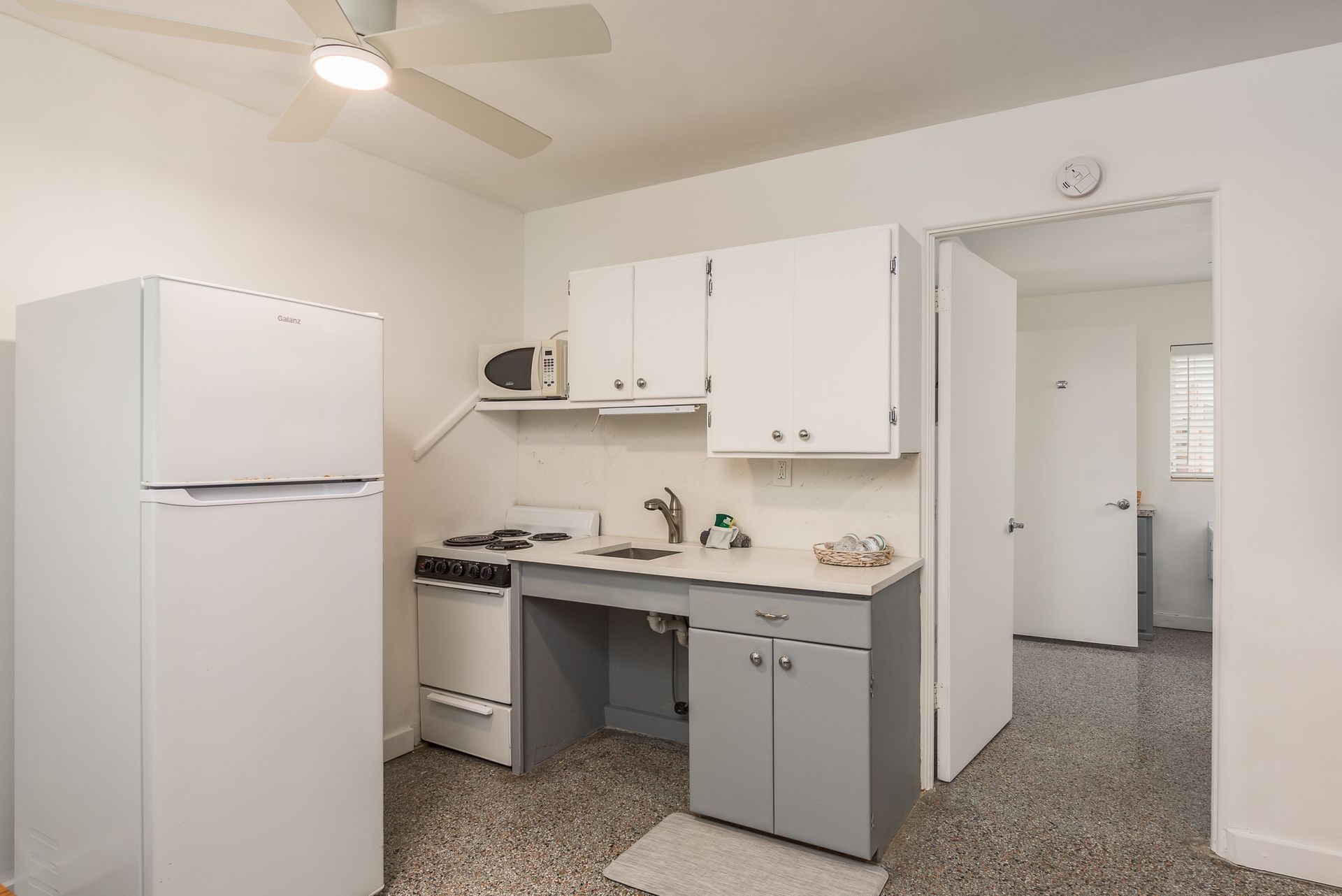 A kitchen with a refrigerator , stove , sink and ceiling fan.