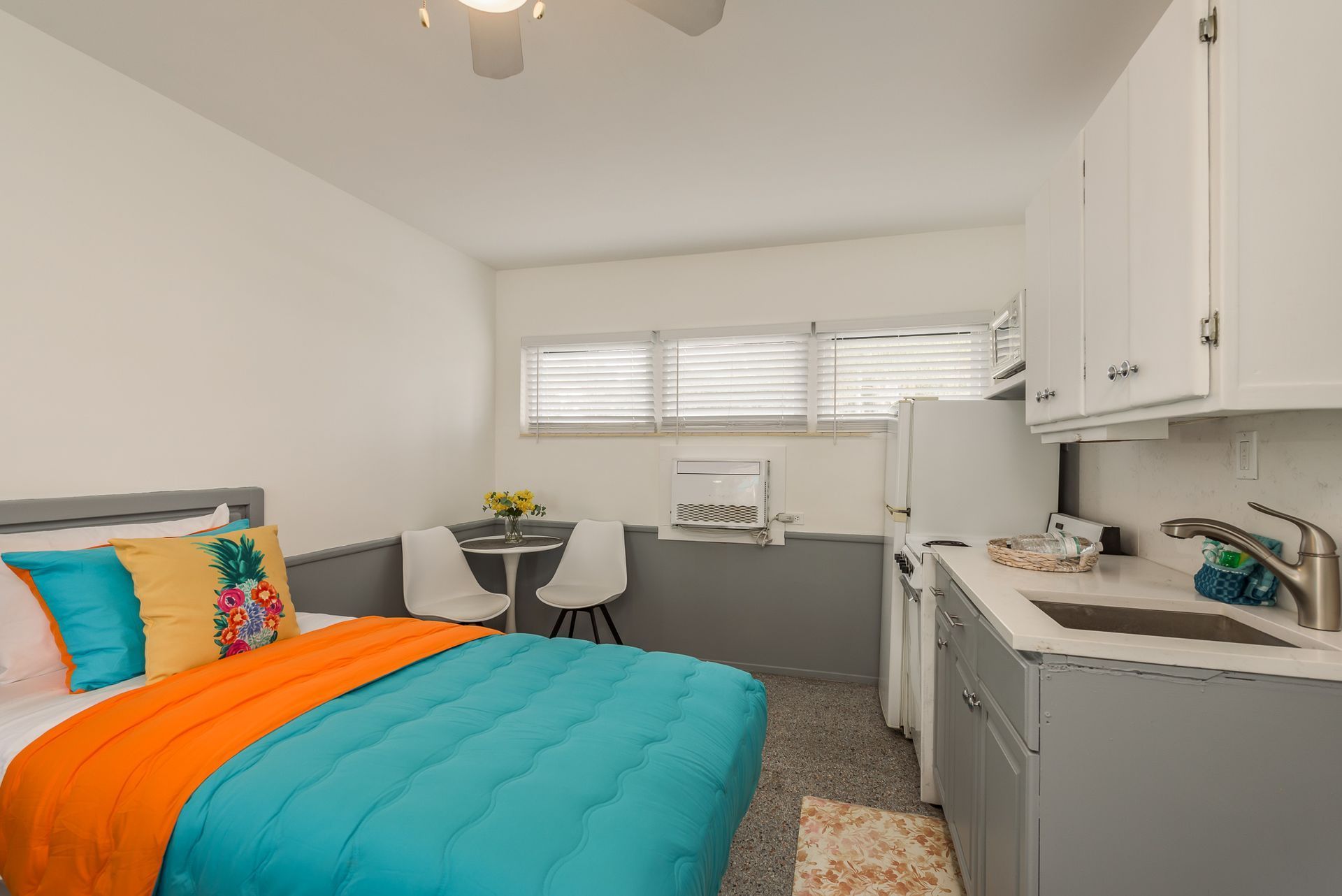 A bedroom with a bed , kitchen , desk and chairs.