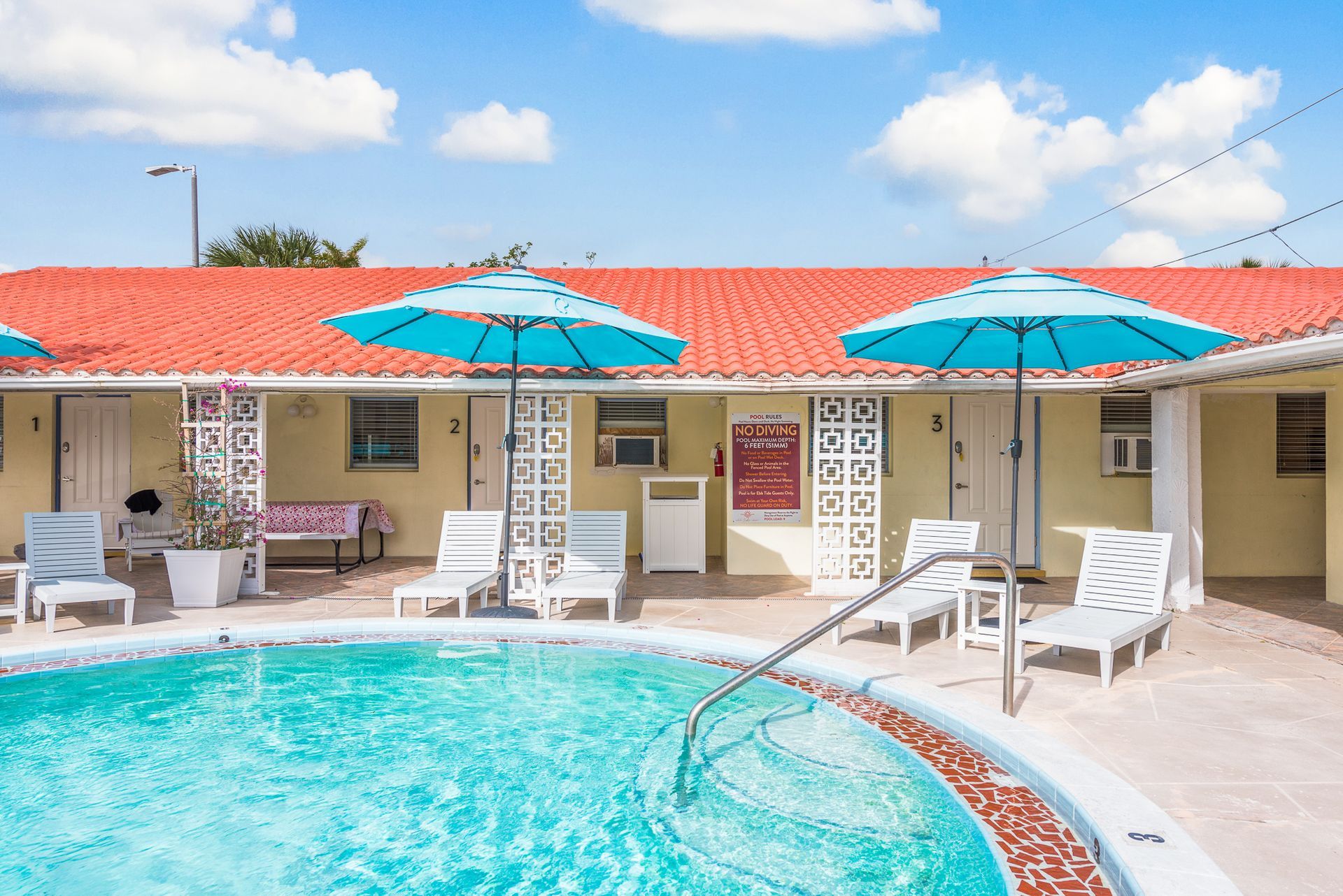 A large swimming pool surrounded by chairs and umbrellas in front of a hotel.