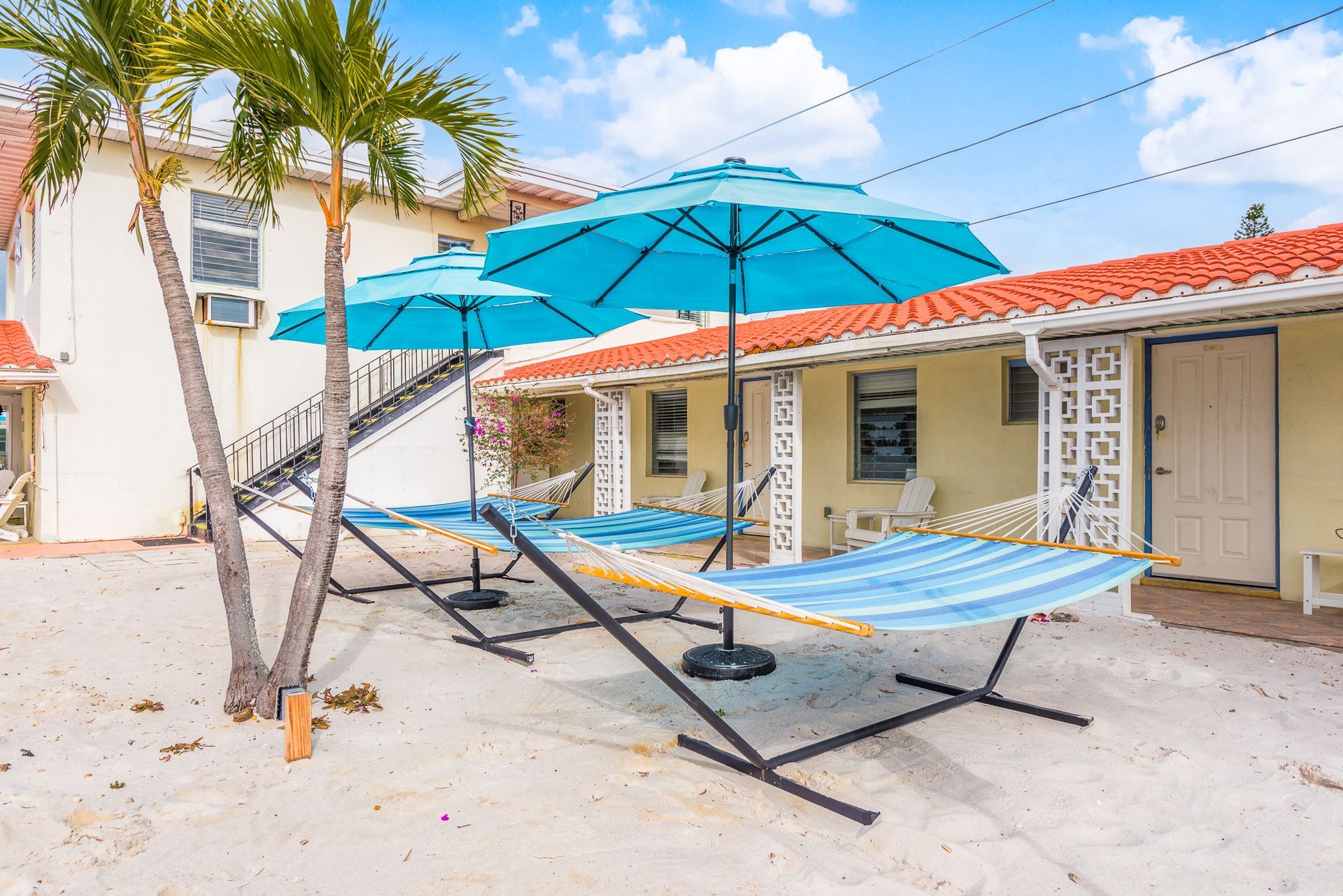 A hammock and umbrellas are sitting on the beach in front of a building.