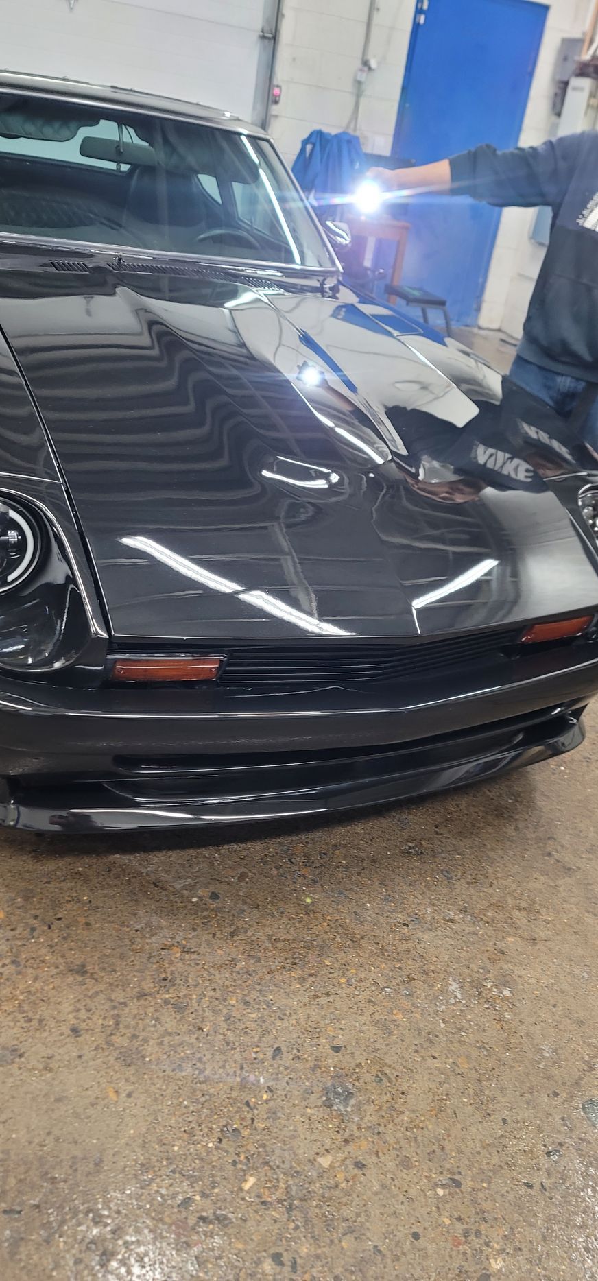 Black car being examined with a flashlight; a person holds the light over the hood.