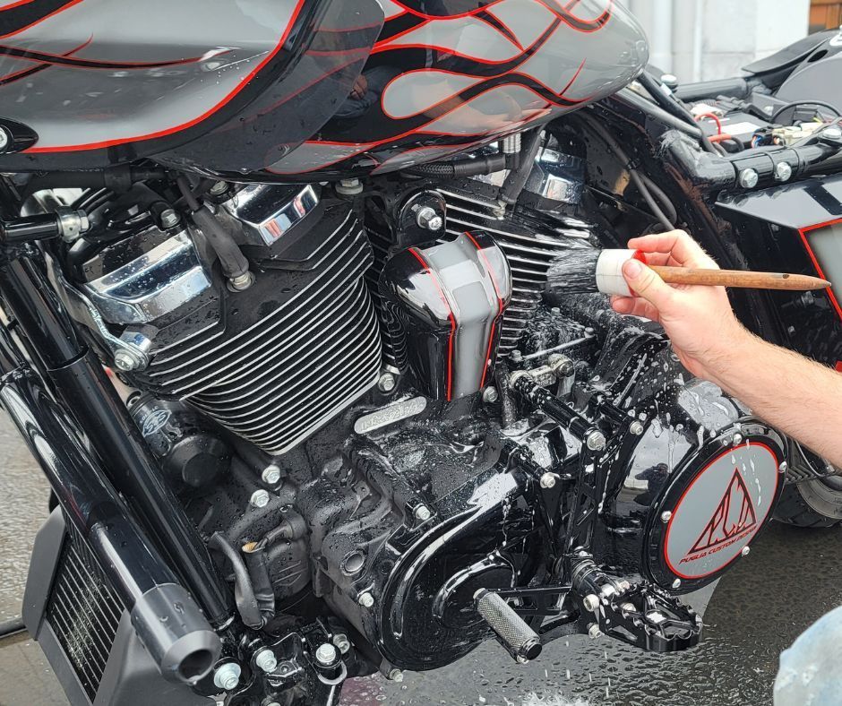 Person washes a motorcycle tire with a soapy sponge on a brick surface.