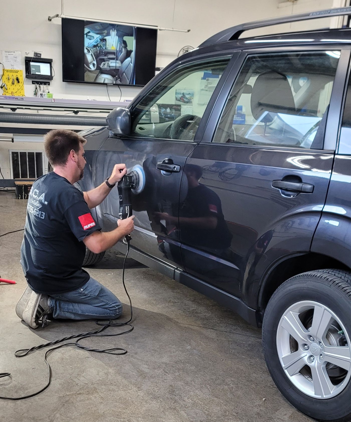 Person polishing a dark car with a power buffer.