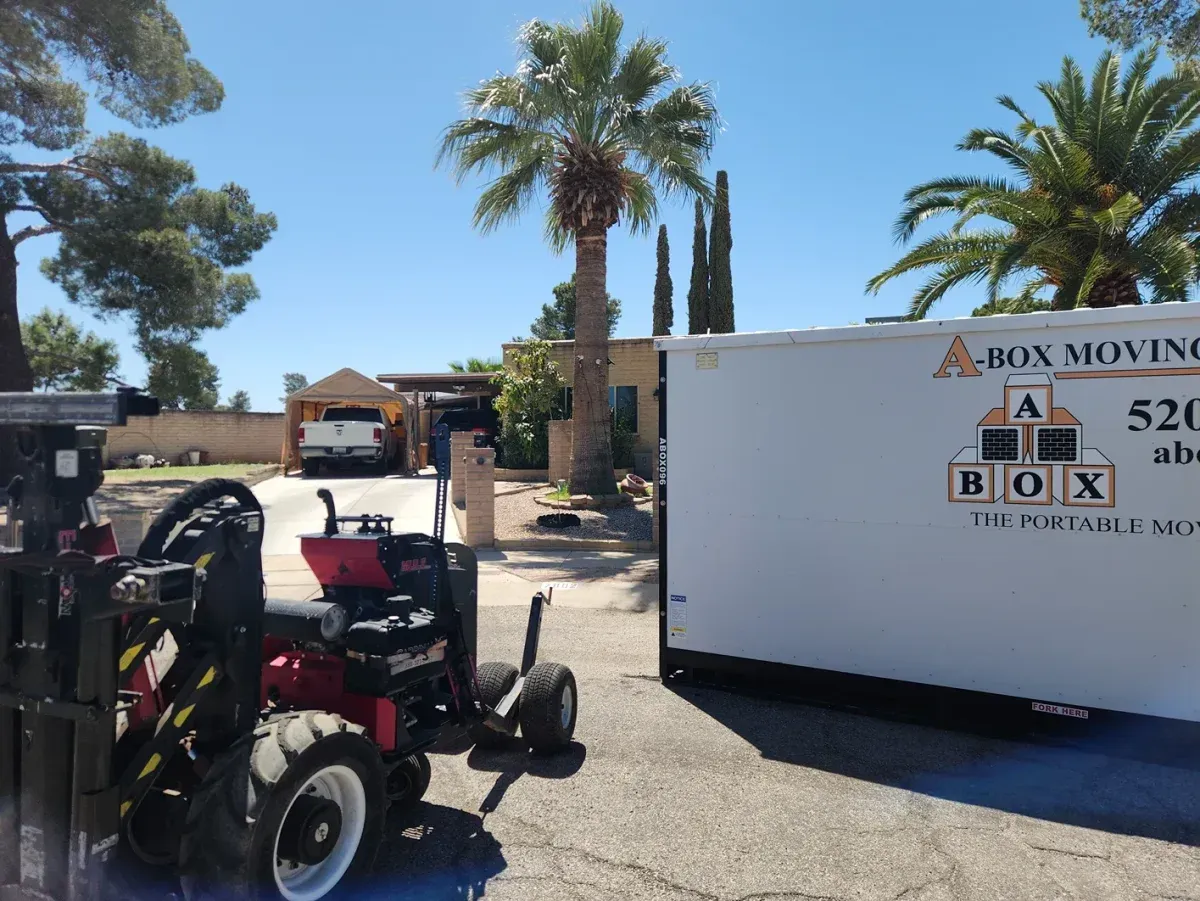 Moving truck and trailer in sunny driveway with palm trees and residential house in background