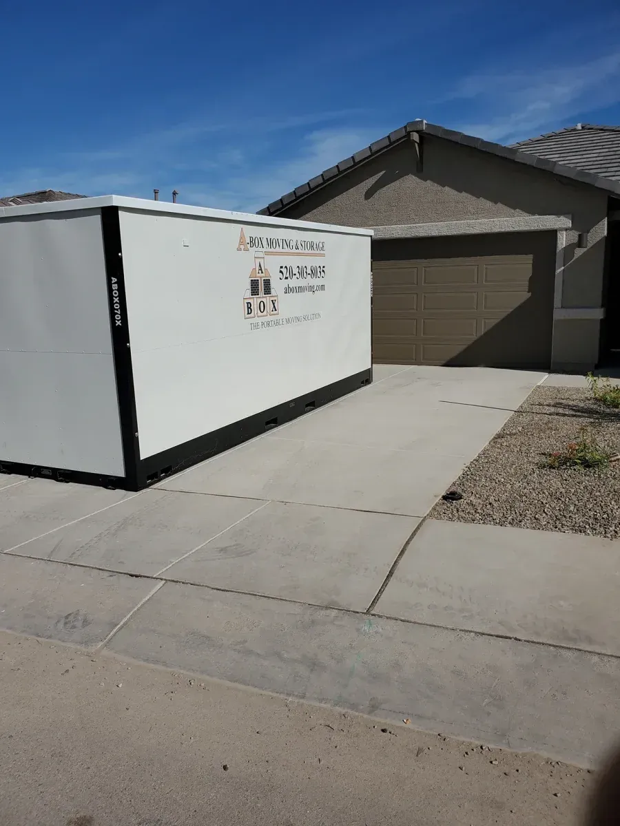 White construction dumpster beside a suburban driveway and garage under a blue sky