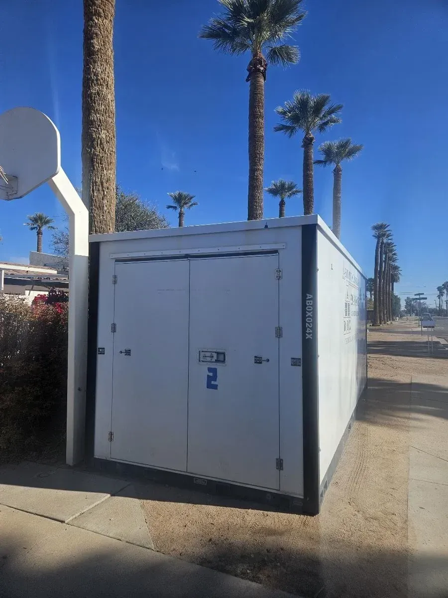 White utility trailer beside a basketball hoop on a sunny palm-lined street