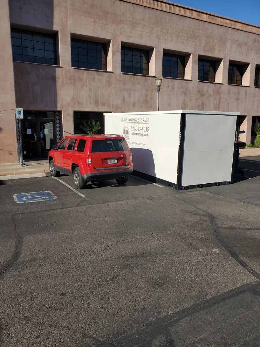 Red SUV parked beside a white storage container outside a brick building