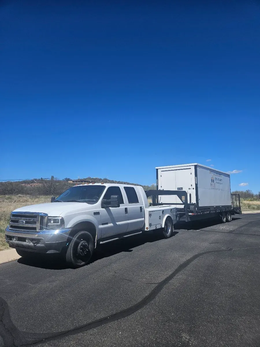 White pickup truck towing a white trailer on a roadside under a clear blue sky