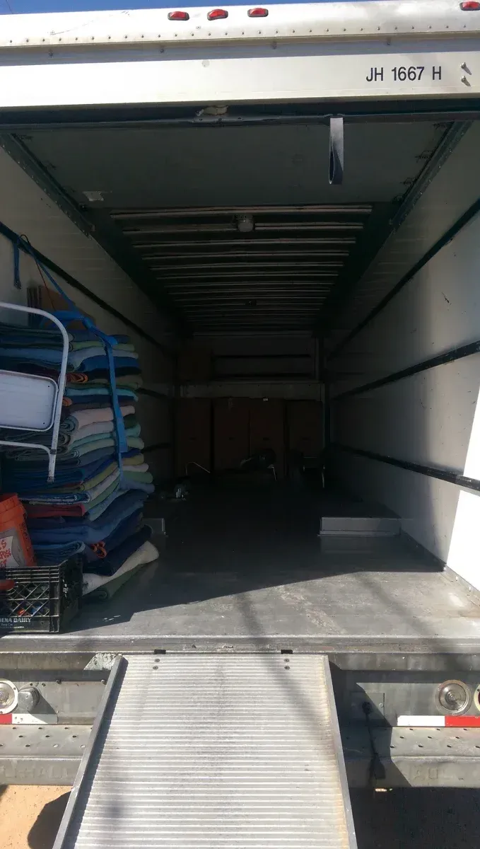 Open truck trailer with ramp lowered, stacked blue goods inside near the left side