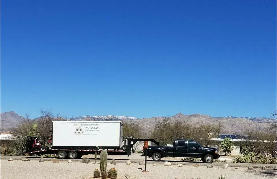 Black pickup truck towing a white trailer through a desert road under a clear blue sky