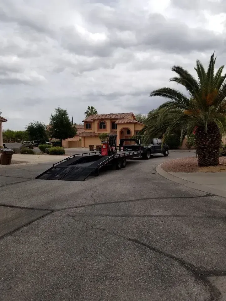 Tow truck with ramp parked on a driveway in front of a tan house under cloudy skies