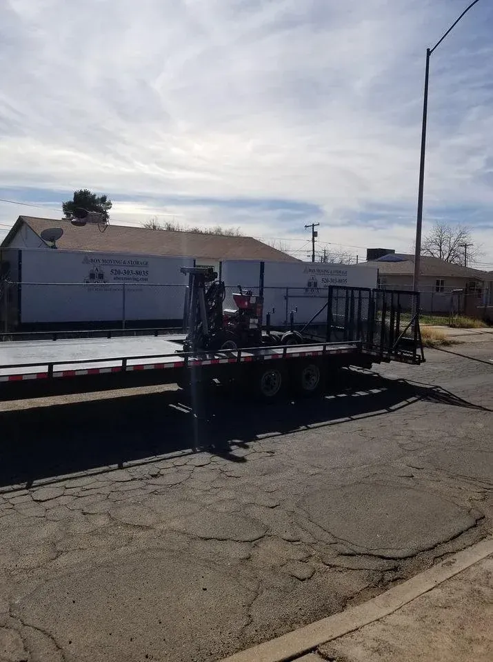 Flatbed trailer parked on a cracked street beside industrial buildings under a cloudy sky