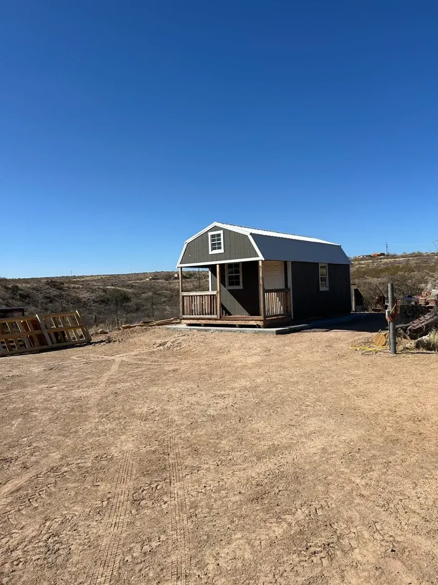 Small gray cabin on a dry, open lot under a clear blue sky