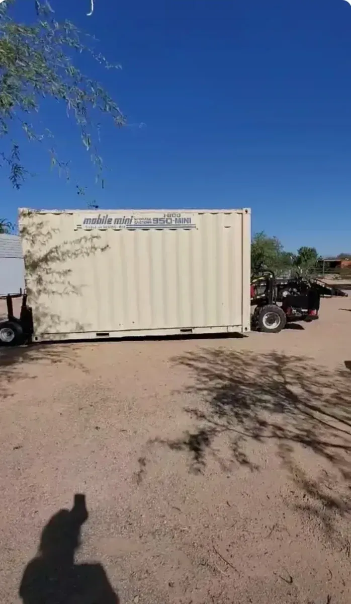 Large beige shipping container truck parked on a dirt lot under a clear blue sky.