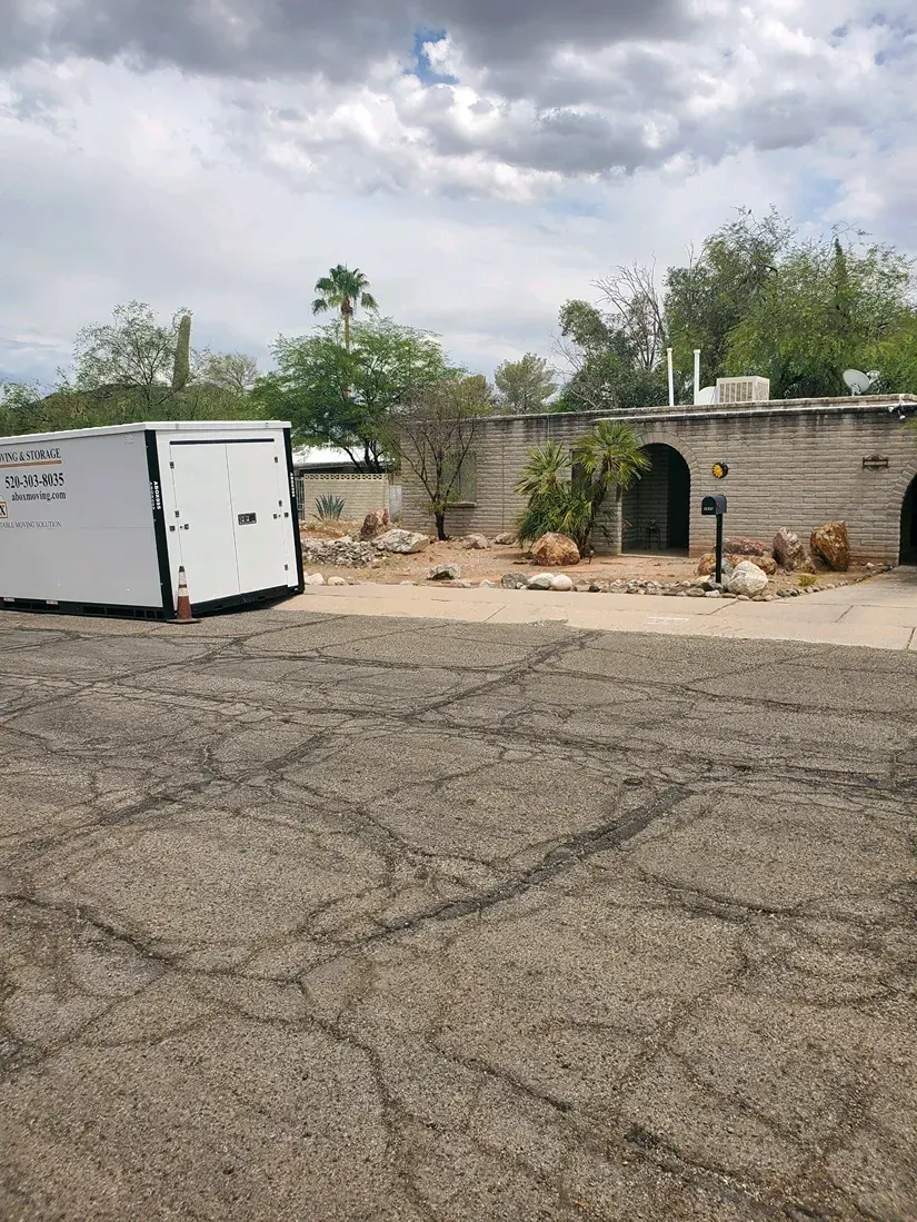 Cracked asphalt lot beside a white trailer and stone wall under a cloudy sky