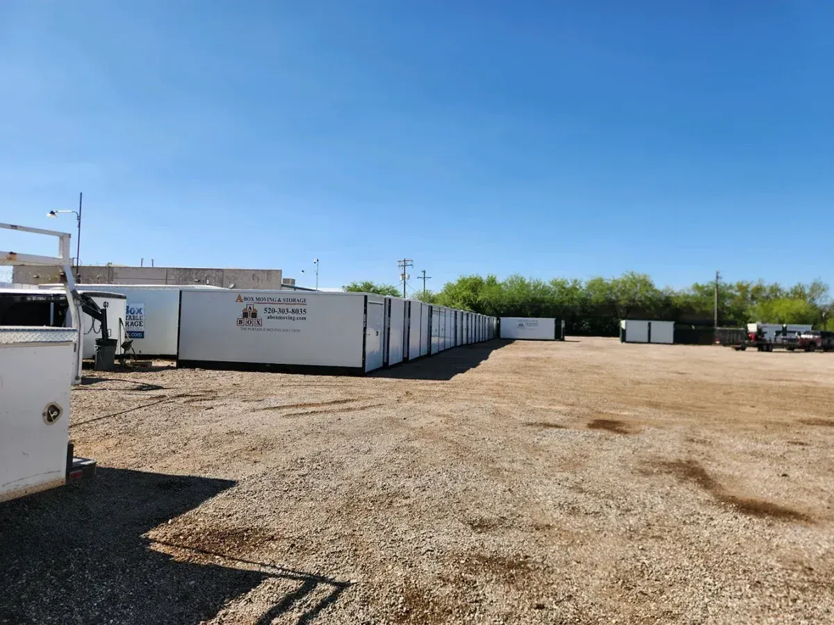 Row of white storage containers in a gravel lot under a clear blue sky