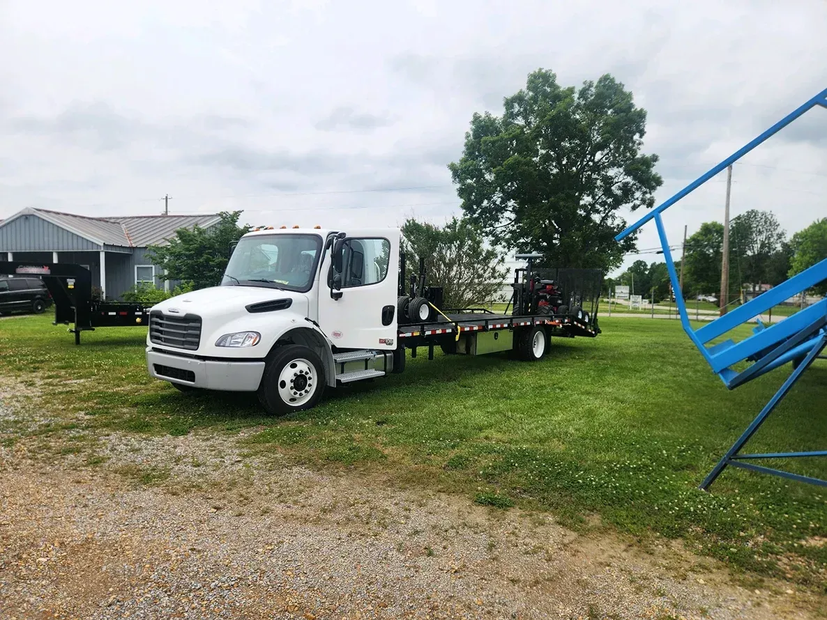 White utility truck parked on grass near a house, carrying a blue metal frame on the back.