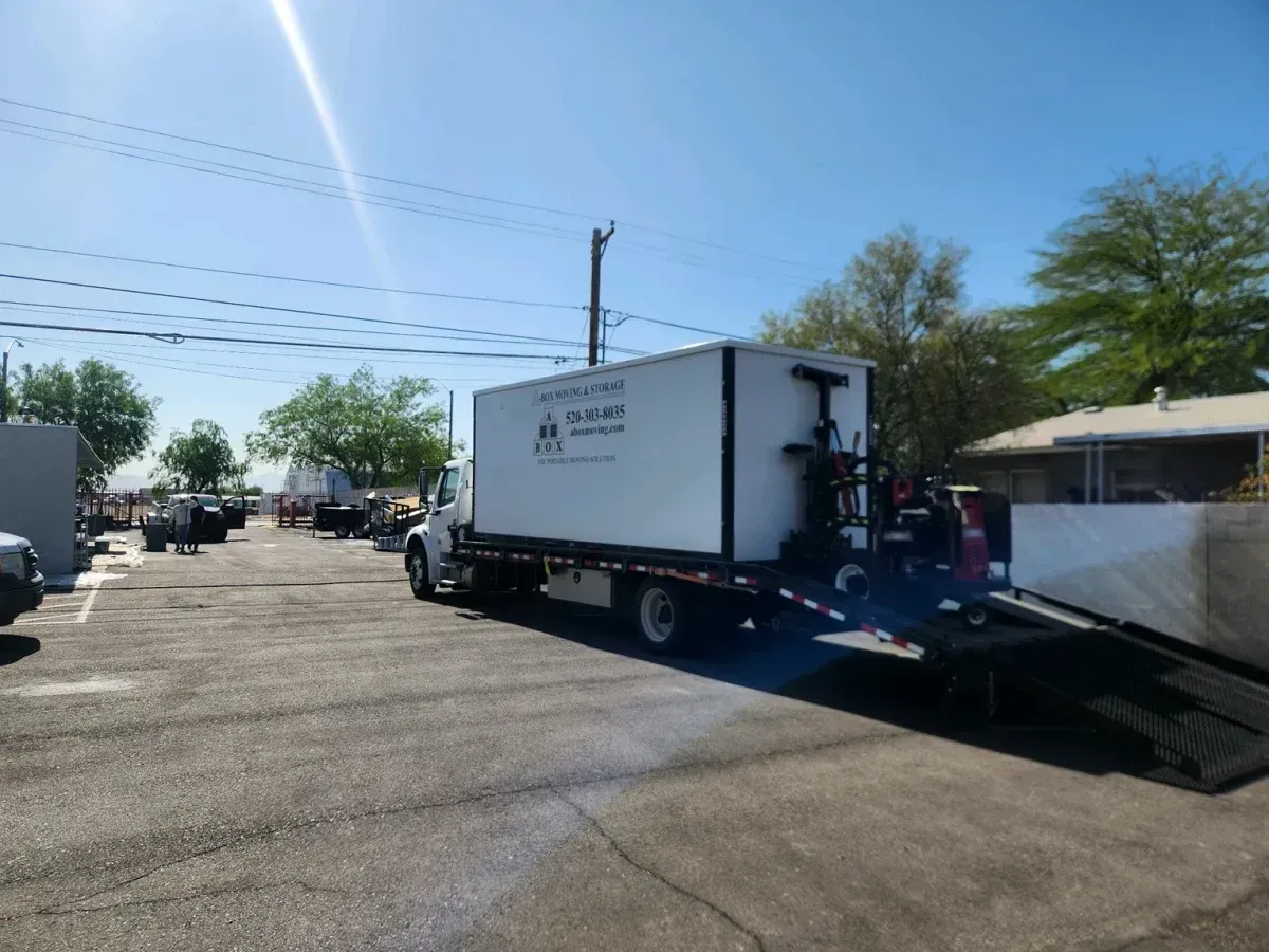 Truck parked on flatbed tow truck in a sunny lot, with another truck and power lines nearby