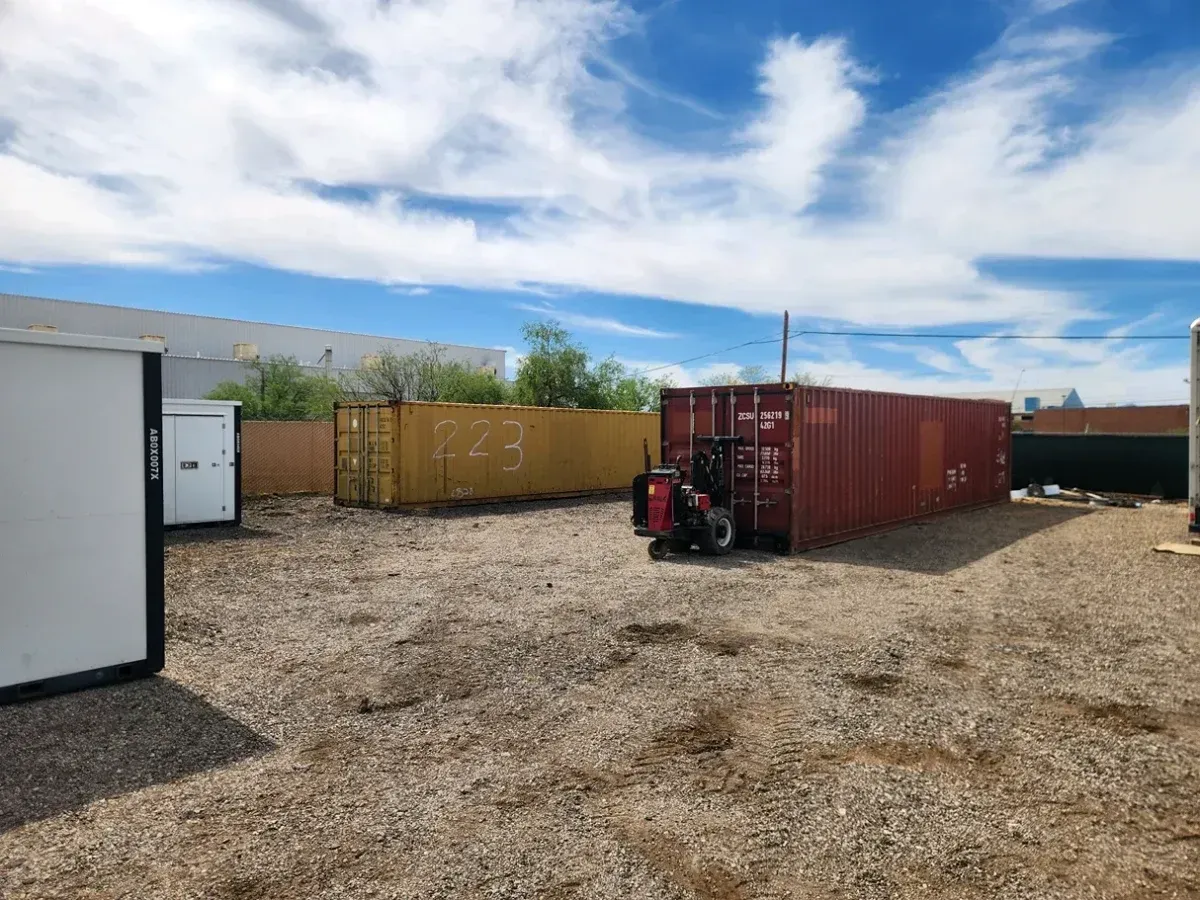 Gravel lot with shipping containers and a forklift under a cloudy sky