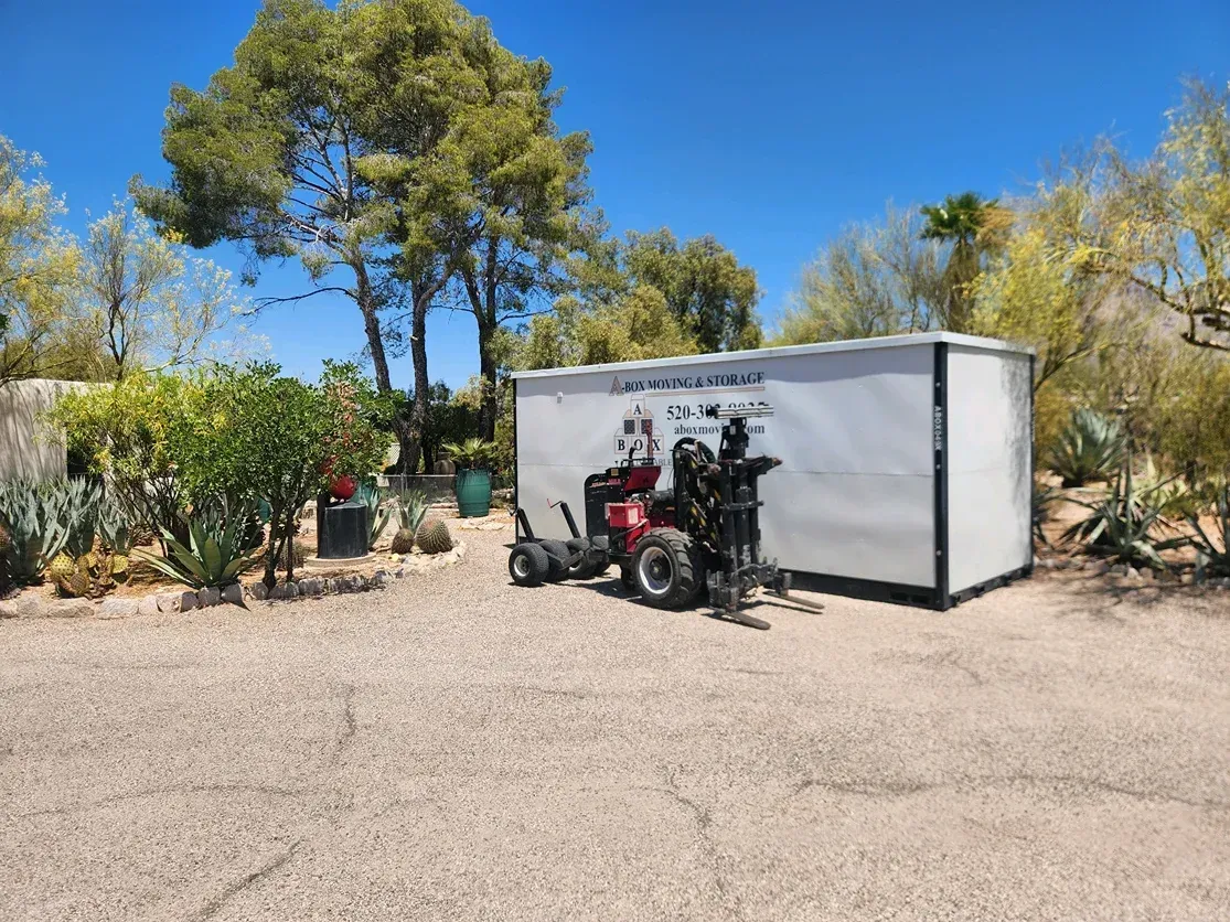 Motorcycle parked beside a white trailer in a sunny gravel yard with trees and a blue sky