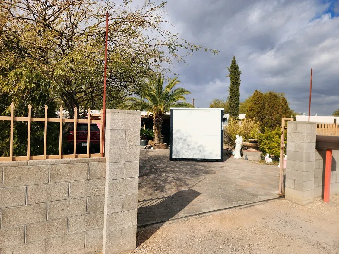 Open gate and driveway with a white gate panel, stone walls, and trees in the background