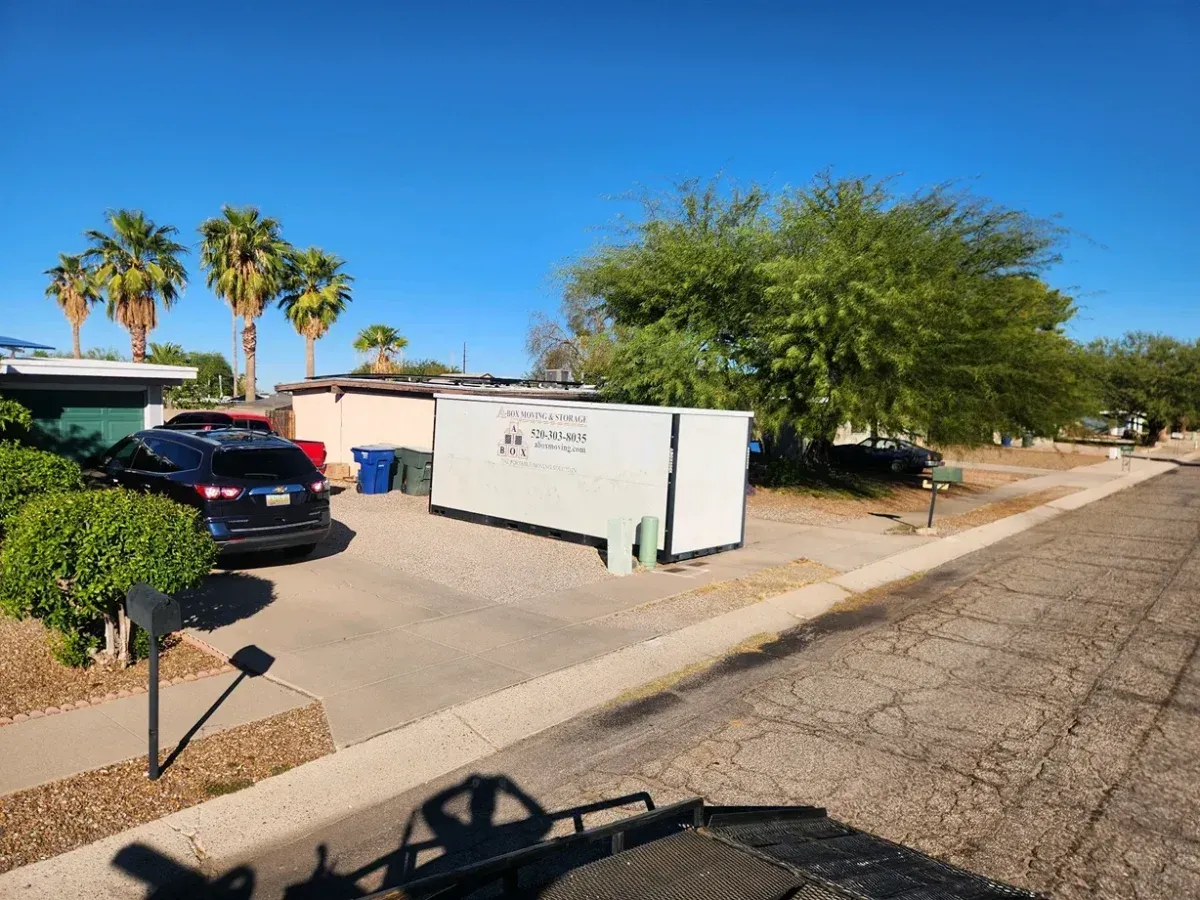 Residential street with parked cars, a white utility box, trees, and clear blue sky.