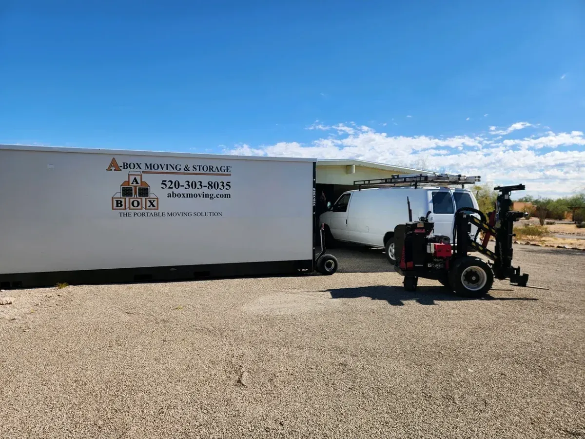 White box truck and forklift in a gravel lot under a blue sky