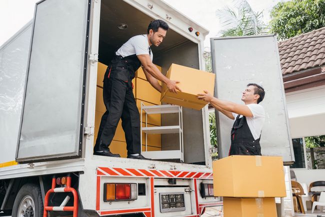 Movers passing cardboard boxes between a truck and a home driveway