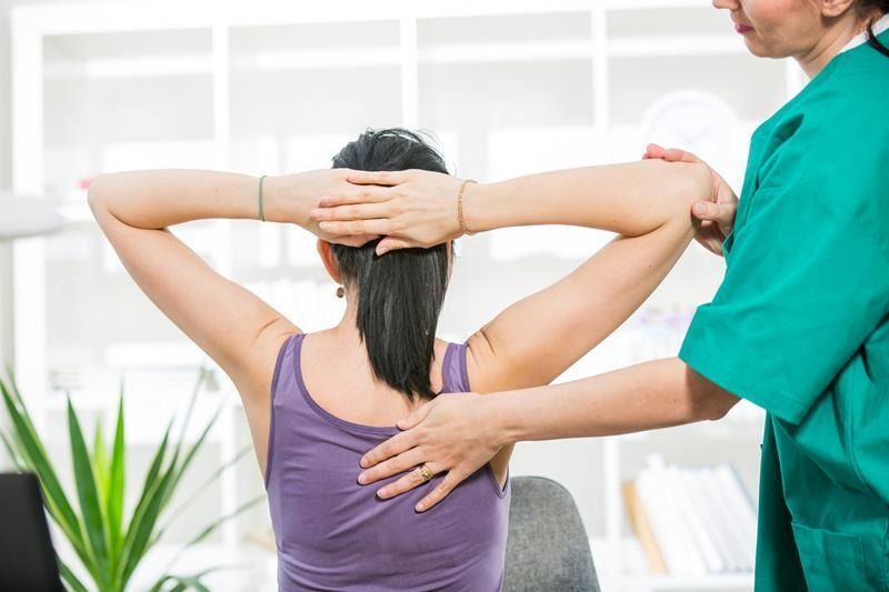 Physical therapist assisting a client stretching her shoulders in a bright clinic