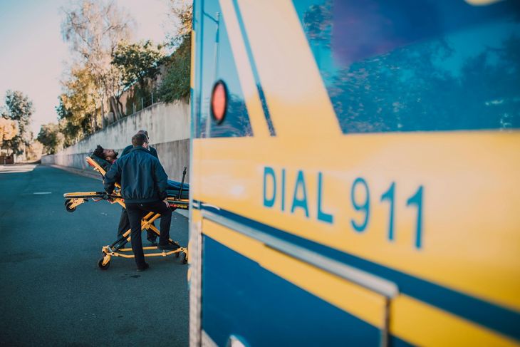 Ambulance with “DIAL 911” beside a person pushing a stretcher on a road