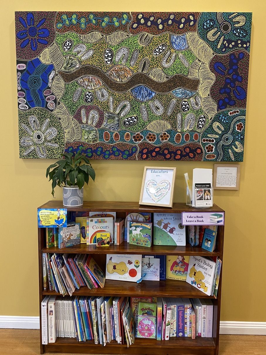 A Bookshelf Filled With Books And A Painting On The Wall — Juniors At Wamberal in Wamberal, NSW