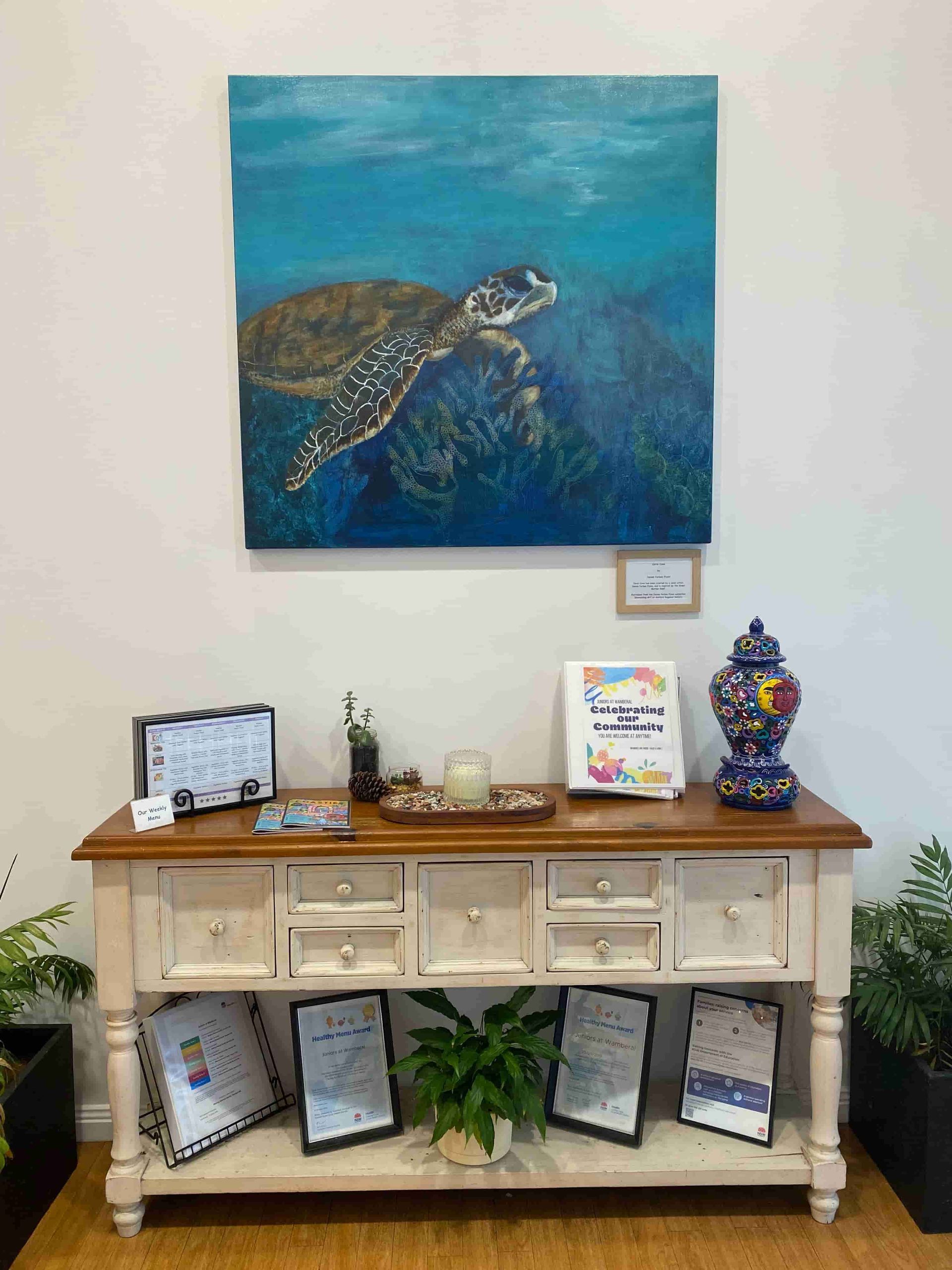 A Painting Of A Sea Turtle Is Hanging On A Wall Above A Table — Juniors At Wamberal in Wamberal, NSW
