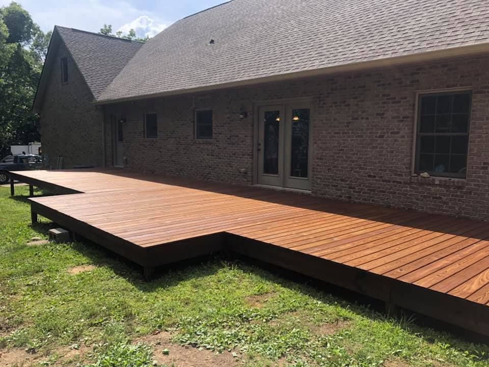 A large wooden deck is in front of a brick house.