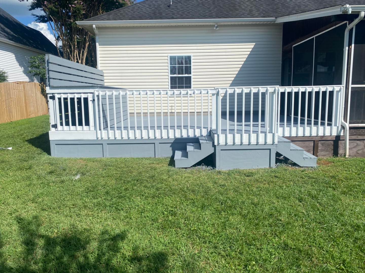 A white house with a gray deck and stairs in front of it.