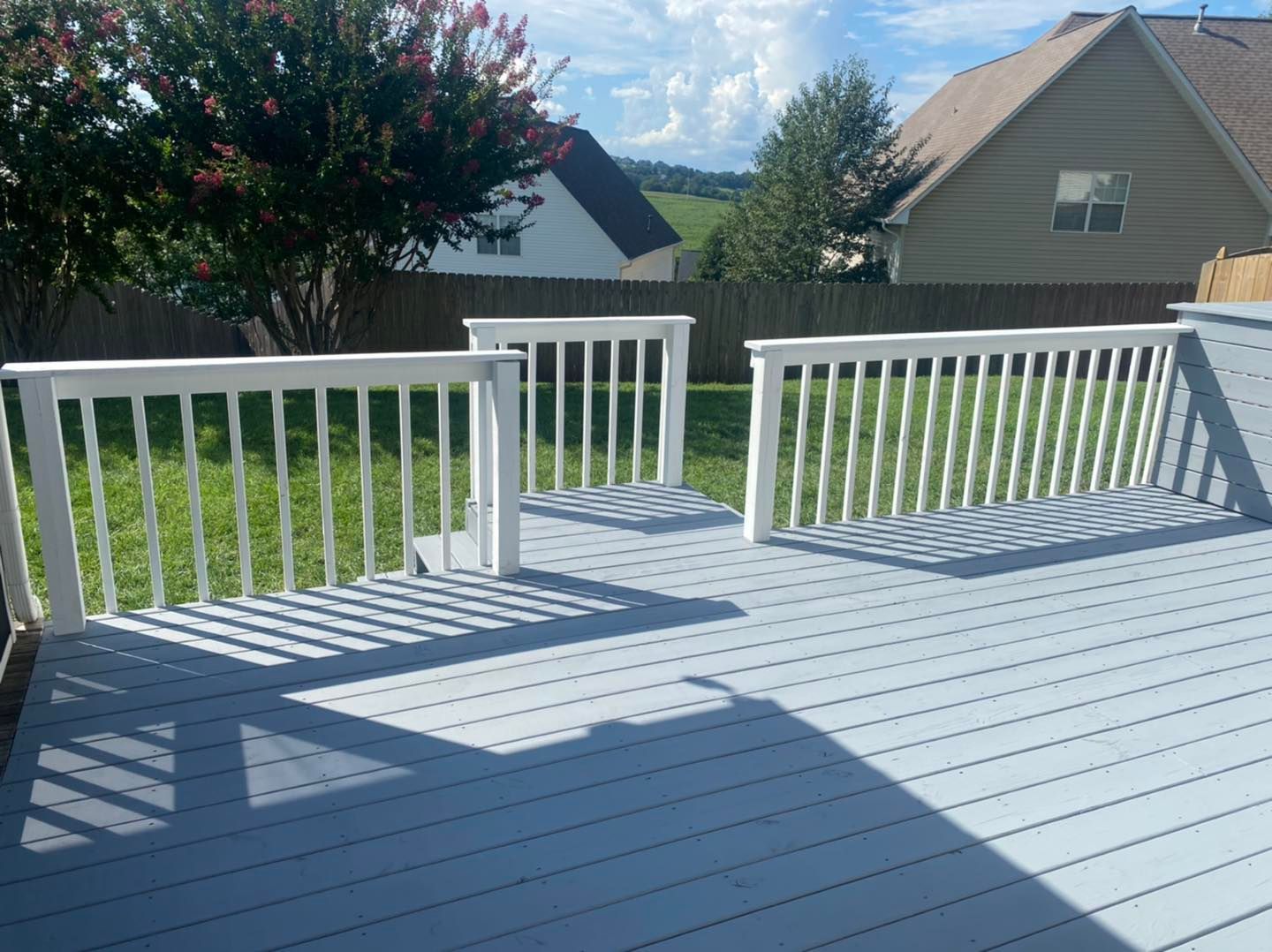 A deck with a white railing and a house in the background