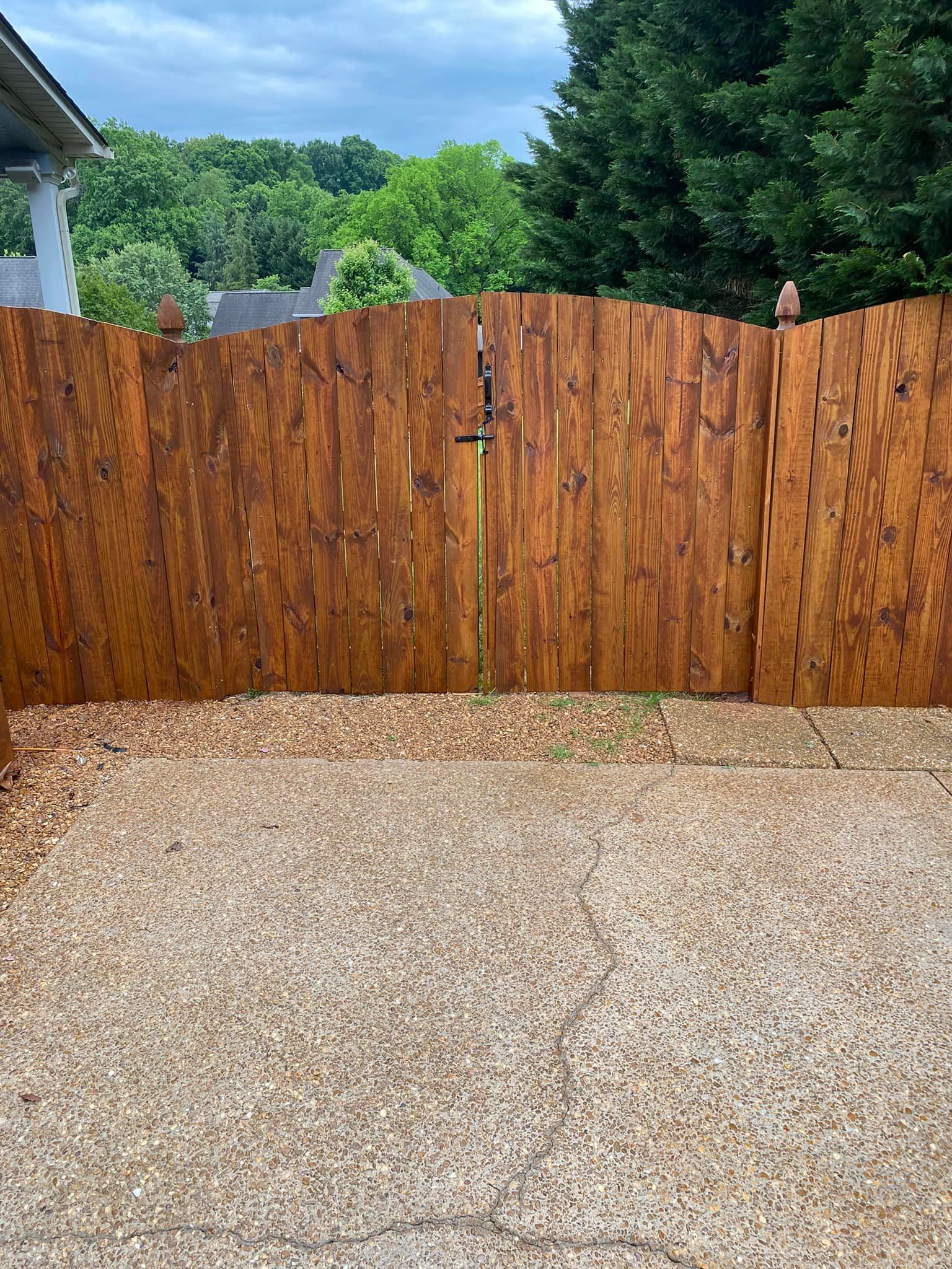A wooden fence surrounds a gravel area in a backyard.