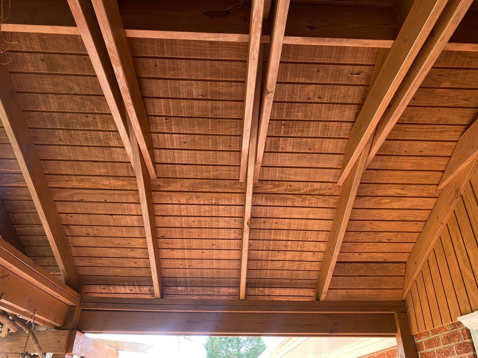 The ceiling of a wooden structure with a brick wall in the background.