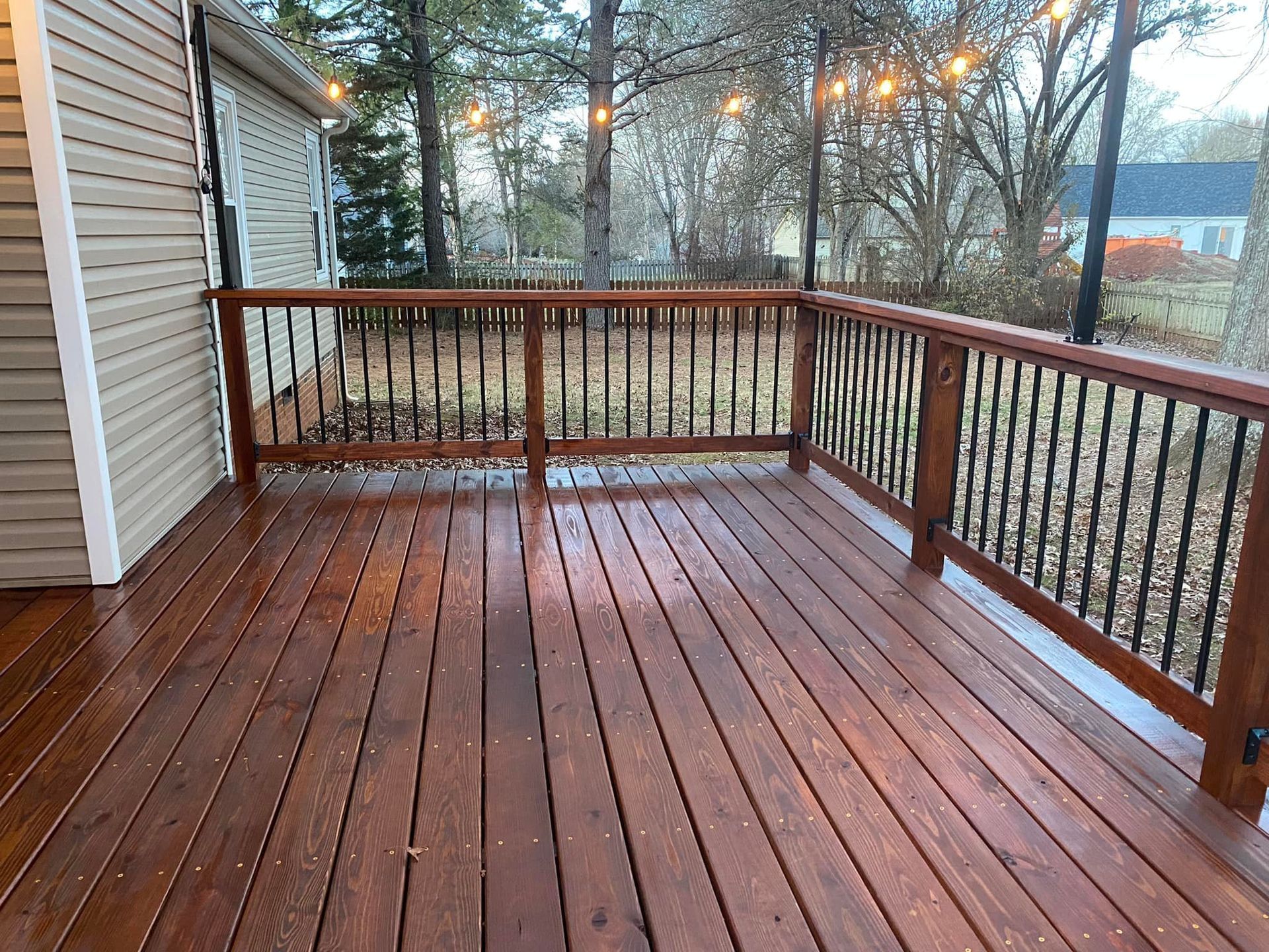 A large wooden deck with a metal railing and a house in the background.