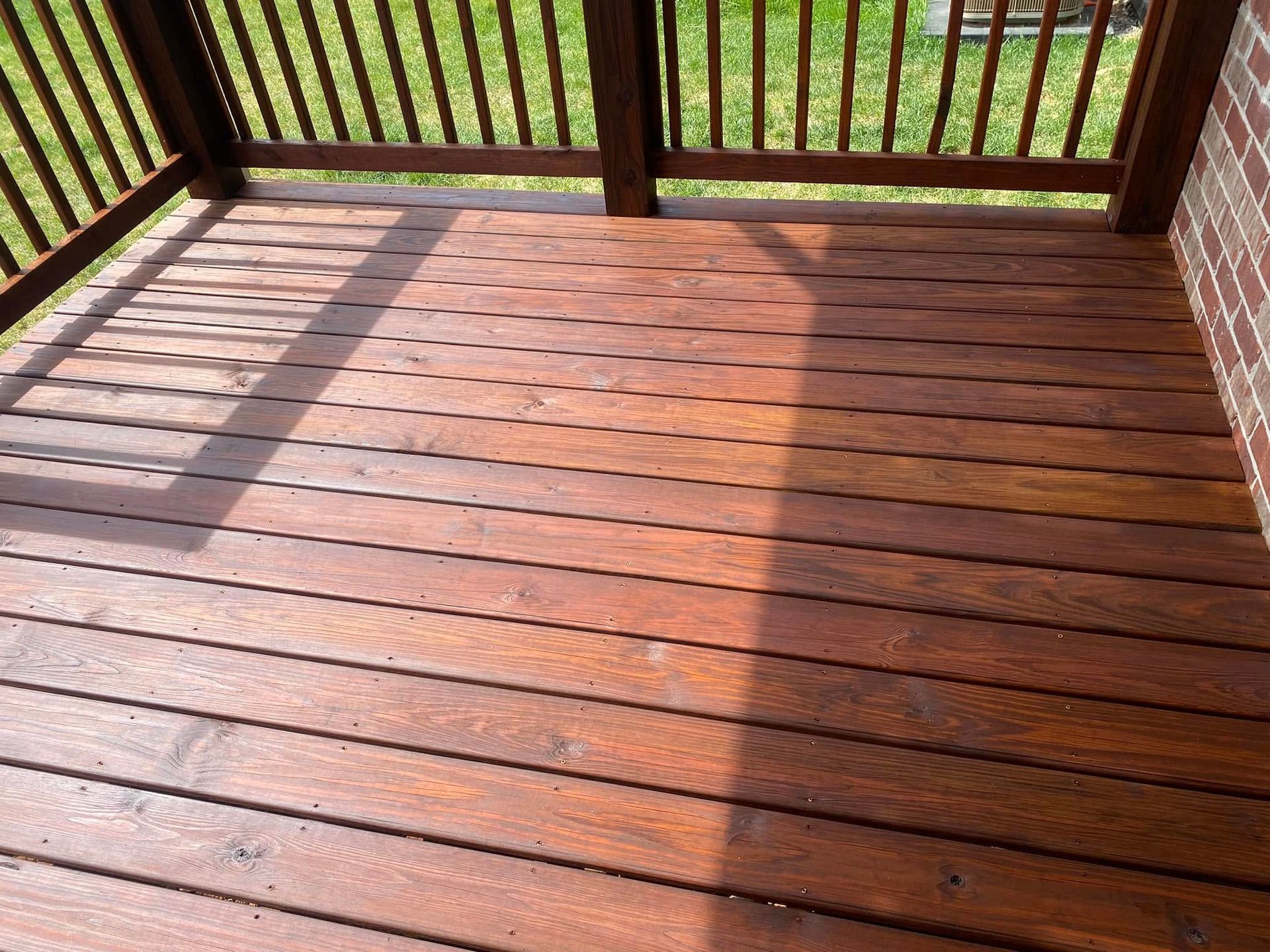 A wooden deck with a railing and grass in the background.