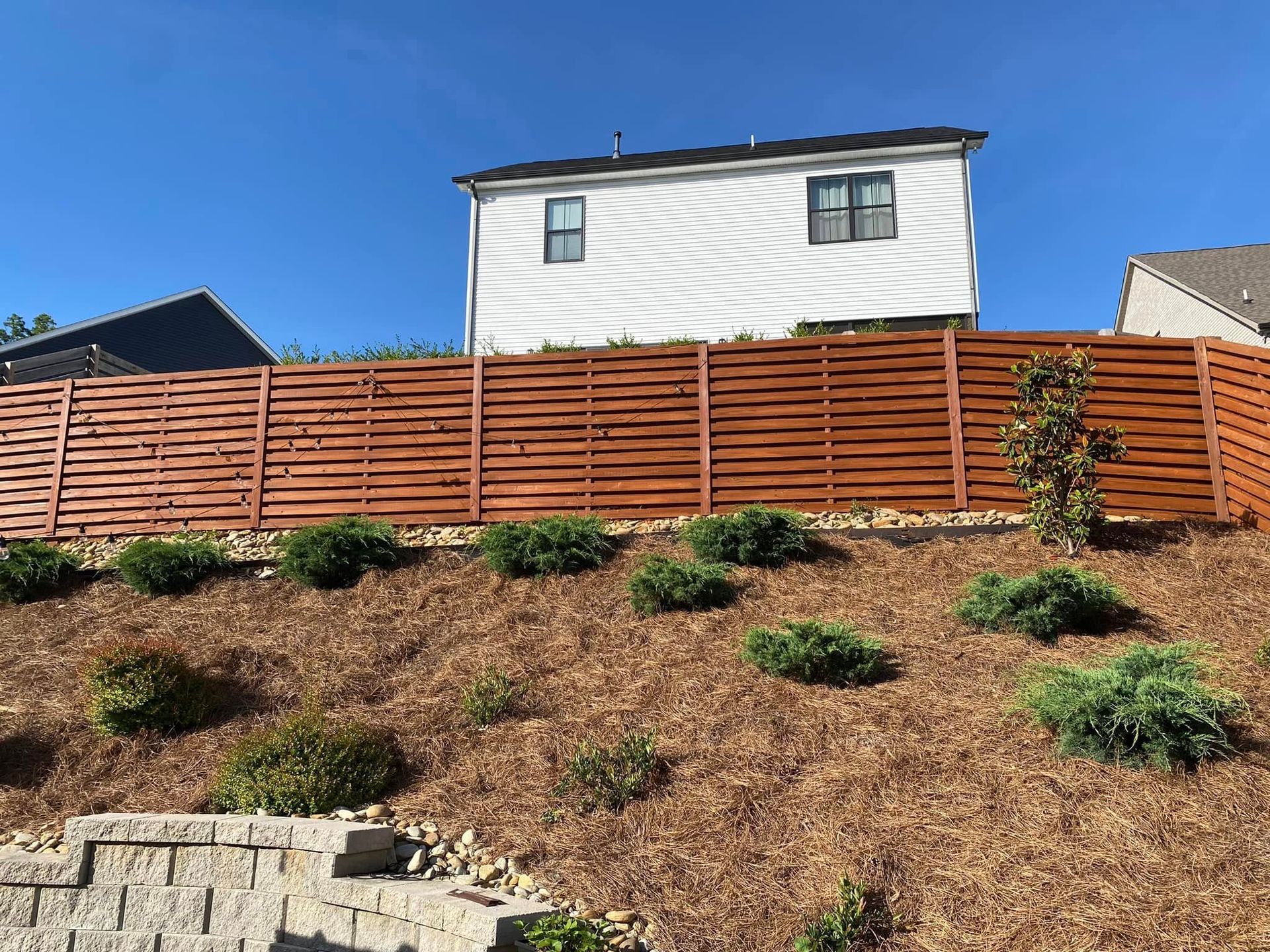A wooden fence surrounds a house on a hill.