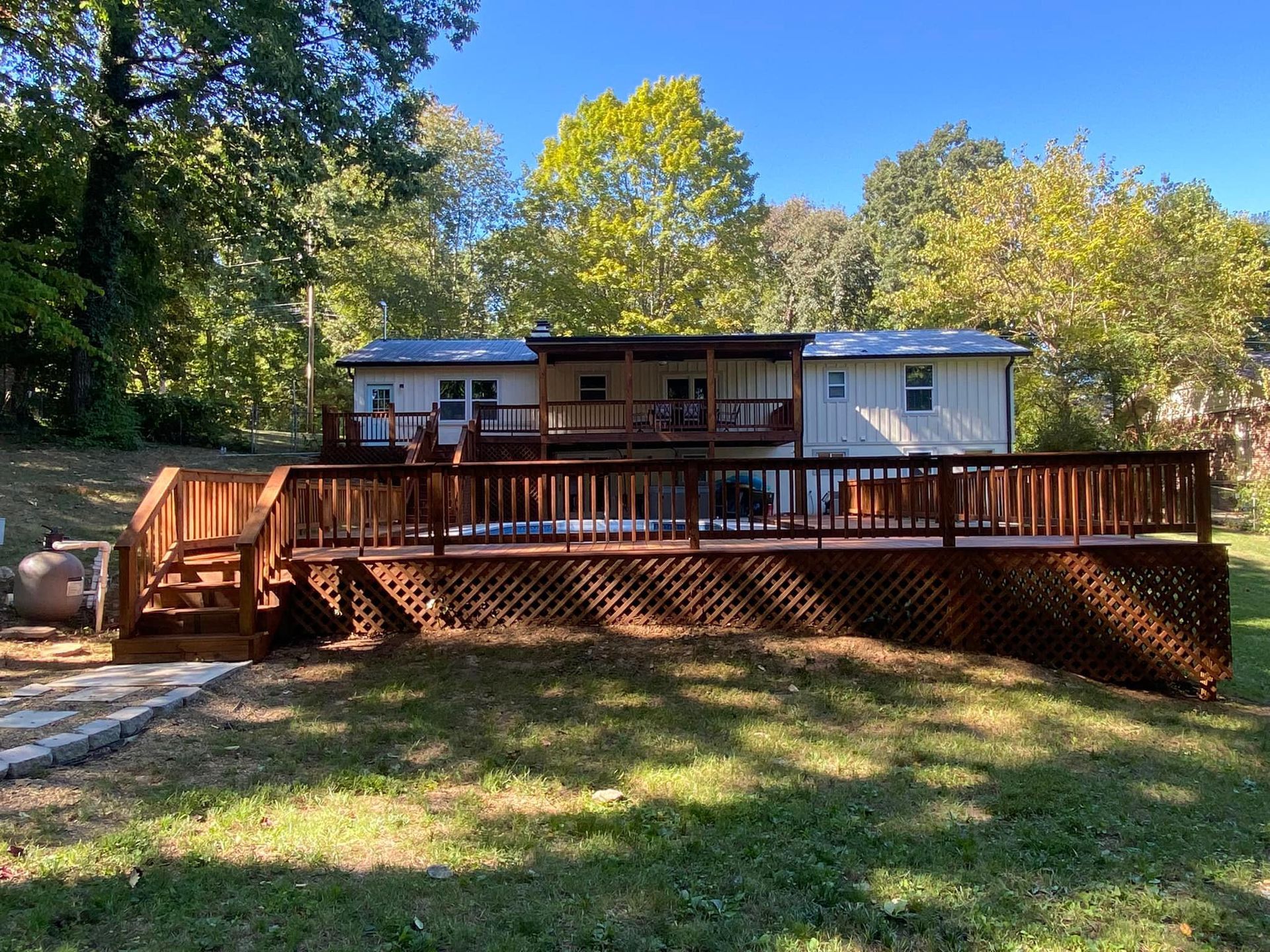 A large wooden deck is in front of a house surrounded by trees.